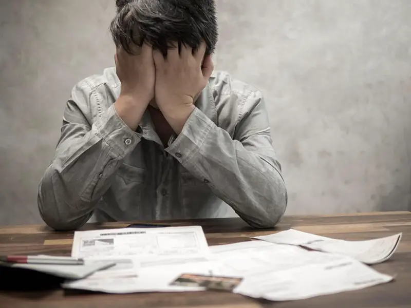 stress man with his hands covering his face, in front of him are papers