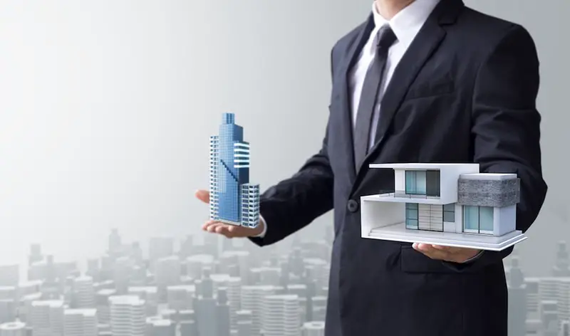 a businessman holding miniature house and building by his both hands