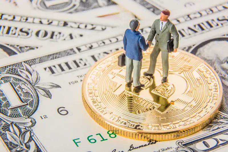 Two miniature businessmen shaking hands while standing on bitcoin cryptocurrency