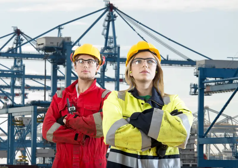 Two tough looking dockers in safety clothing posing in front of a huge container terminal