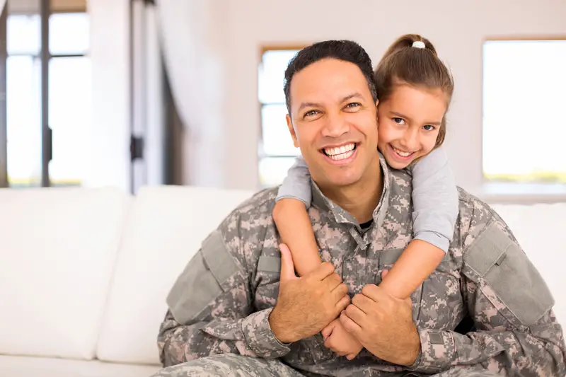 a military father hugs from the back by his daughter