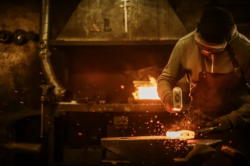 The blacksmith forging the molten metal on the anvil in smithy.