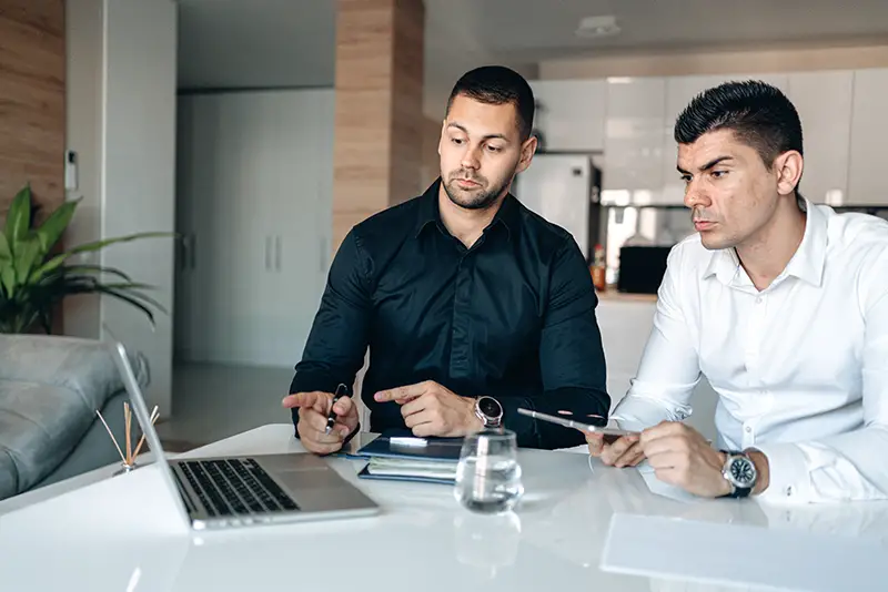 two businessmen having conversation holding pen and macbook pro