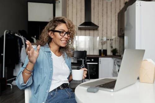 a girl holding a mug talking via video call on her laptop