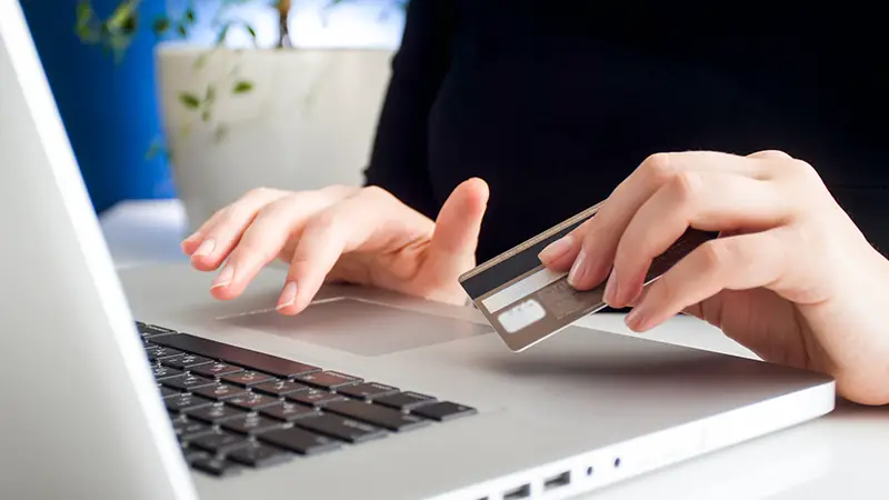 Hand of woman typing on laptop while holding credit card