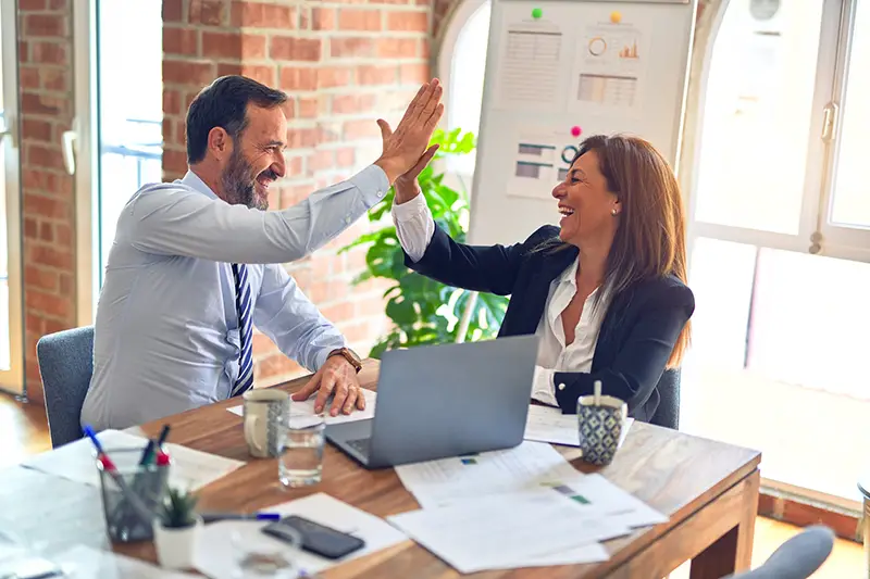 Two middle age business workers with smile on face hand giving high five at the office