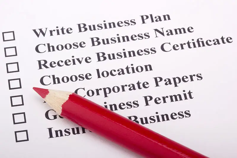 A red pencil laying on a paper with a checklist for starting a business.