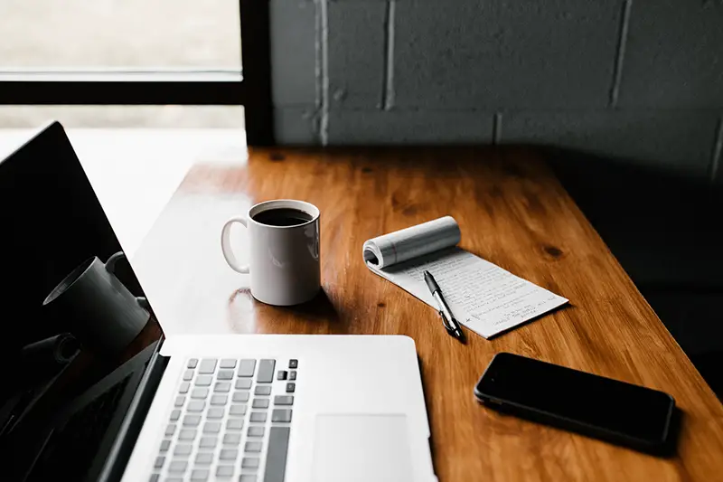 Laptop, white ceramic mug, and smartphone on top of wooden table