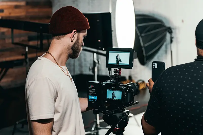 man in white shirt standing in front of black video camera