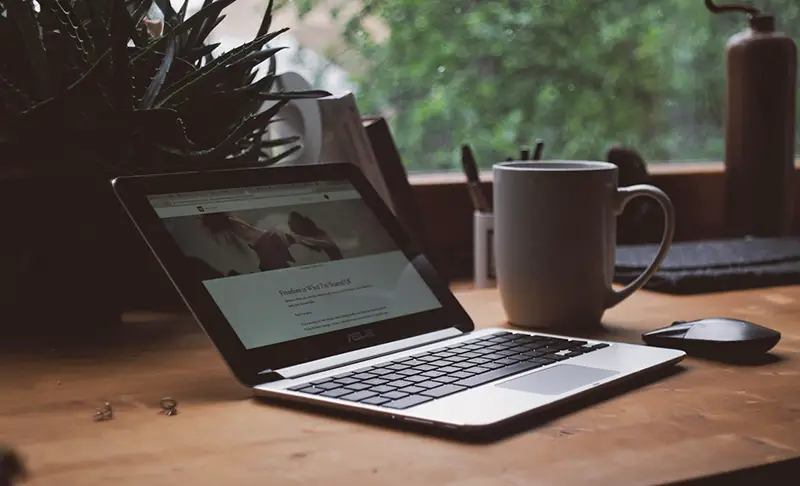 Black and gray Asus laptop near white ceramic mug