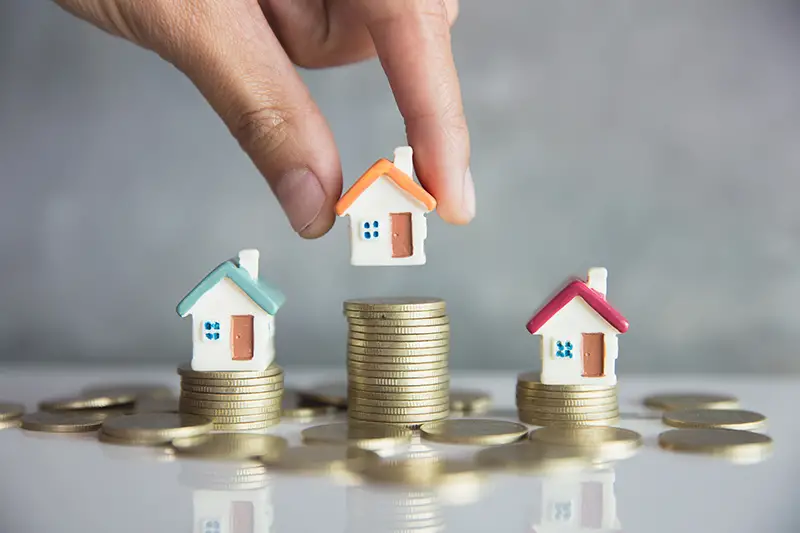 Three Miniature house on top of pile of coins