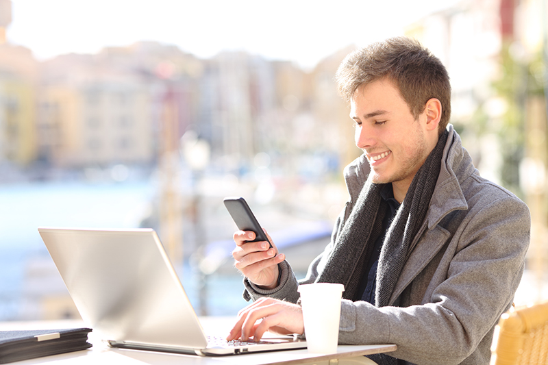 Young man smiling while using his mobile phone and laptop