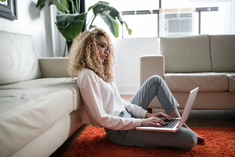 Woman with curly hair sitting in the floor using laptop
