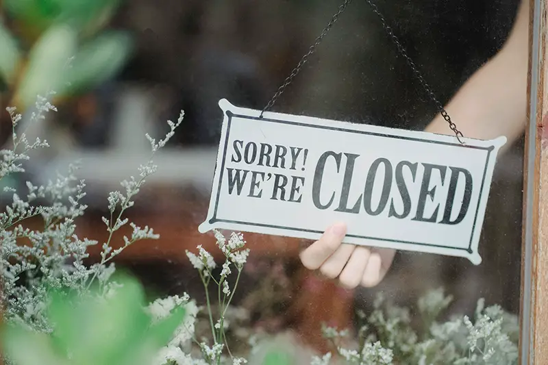 Crop person with we're closed sign board in store