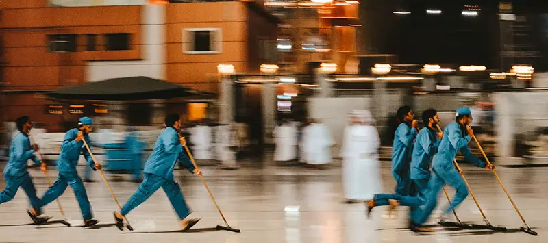 Blue-uniformed cleaners sweep a commercial space