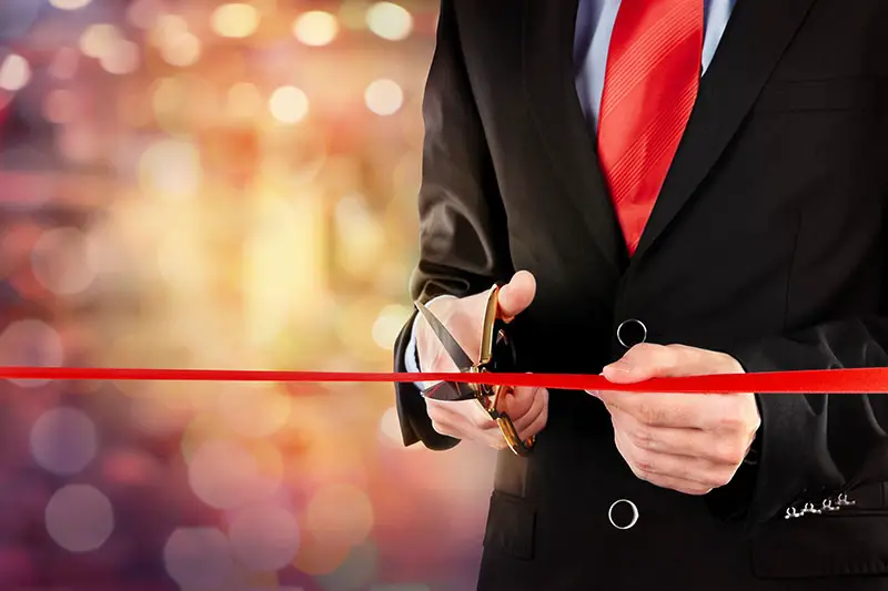 Businessman cutting red ribbon with pair of scissors
