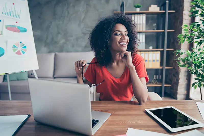 Portrait of pretty cheerful accountant looking away sitting at desk in modern office dreaming about weekend vacation enjoying view from window. Positive thinking person concept