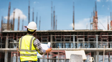 Engineering Consulting People on construction site holding blueprint in his hand.