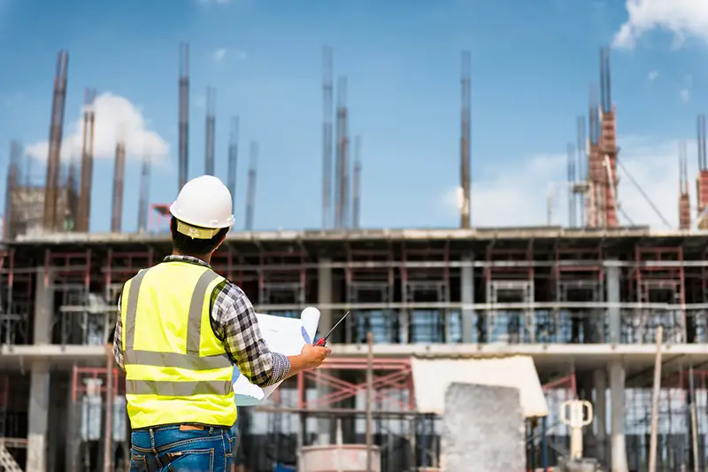 Engineering Consulting People on construction site holding blueprint in his hand.