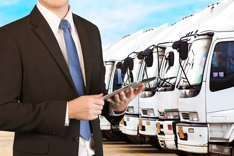 Businessman holding tablet standing over trucks in a row with Container background