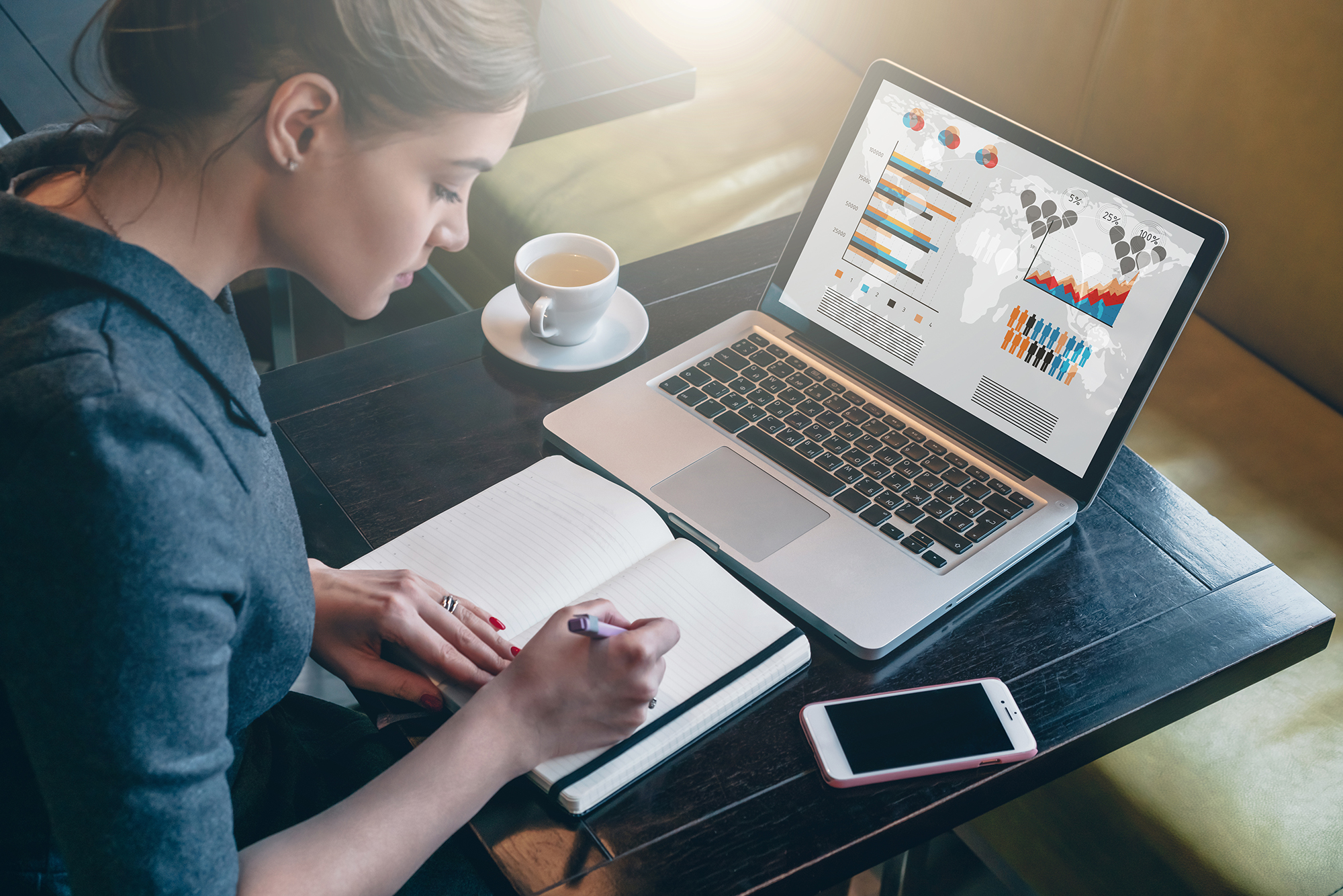 Young business woman sitting at table and taking notes in notebook