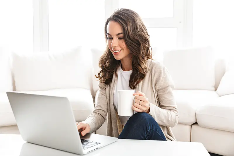 Young smiling woman sitting on the floor while working on her laptop