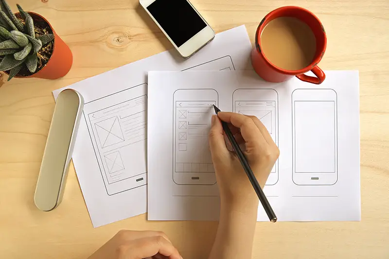 Designer drawing mobile application wireframe on wooden desk