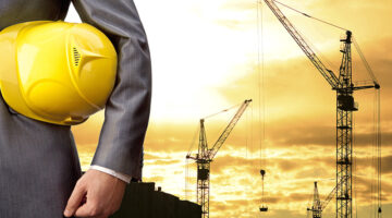 Businessman holding yellow helmet with construction site on the background