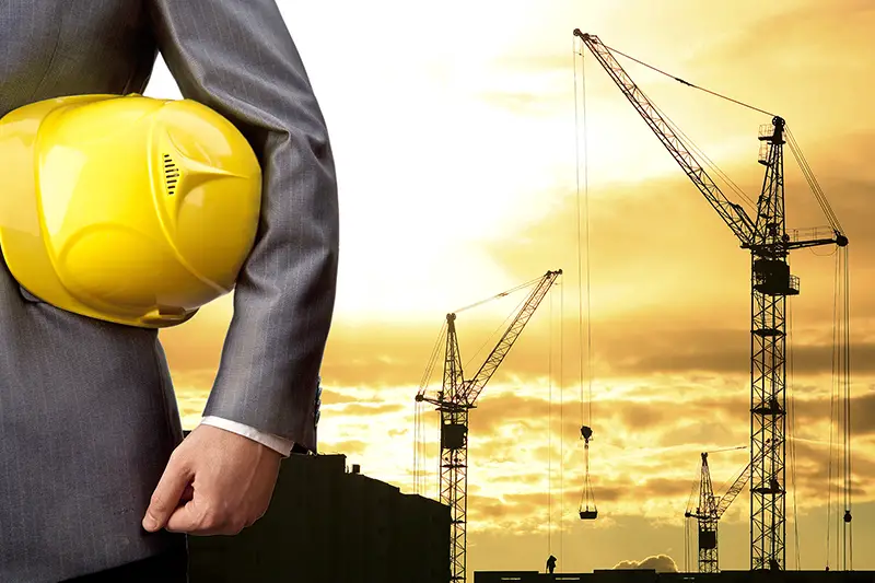 Businessman holding yellow helmet with construction site on the background