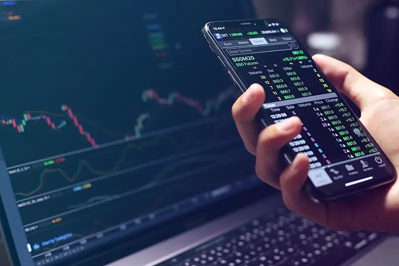 Man using smartphone and laptop for trading