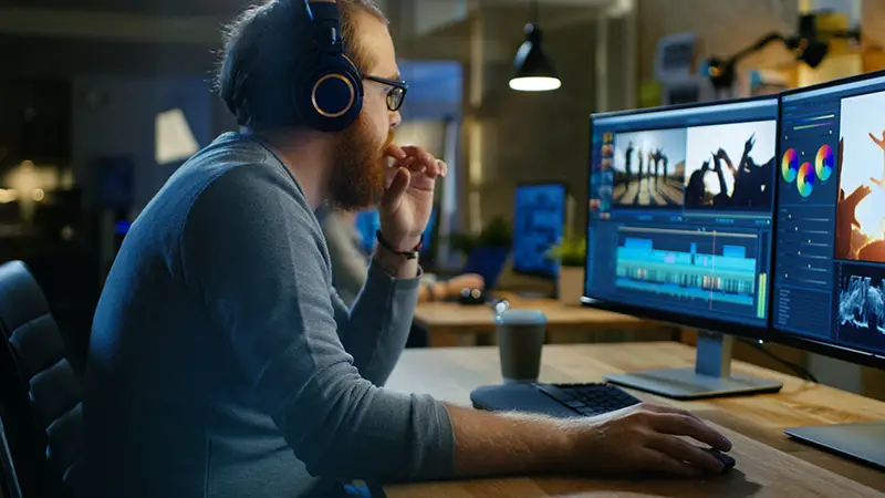 Male Videographer Edits and Cuts Footage and Sound on His Personal Computer, Puts on His Monitors/ Headphones. His Office is Modern and Creative Loft Studio.