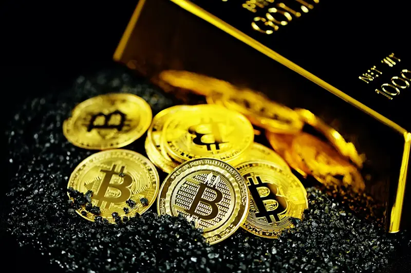 Bitcoins beside gold bar with black sand