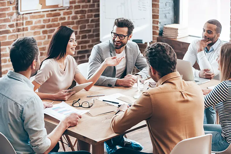 Making great decisions. Young beautiful woman gesturing and discussing something with smile while her coworkers listening to her sitting at the office table