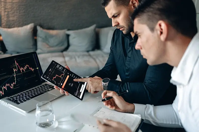 Two businessman in front of laptop with trading chart on the screen