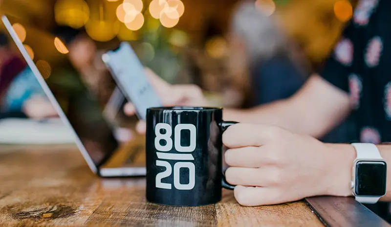 Person holding black coffee mug with 80/20 number printed