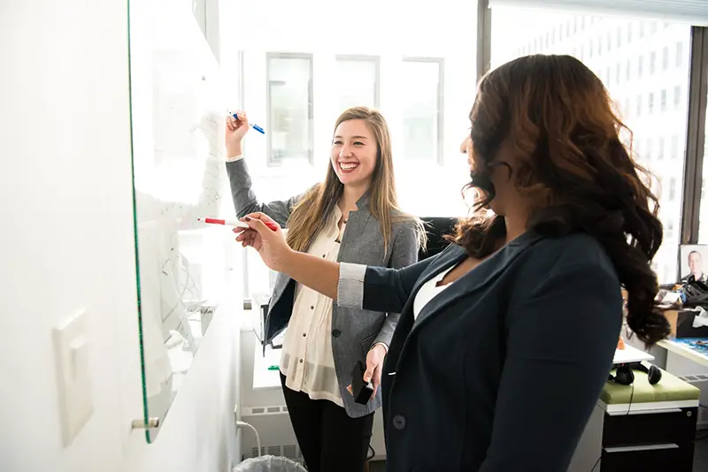 Two women in front of white board