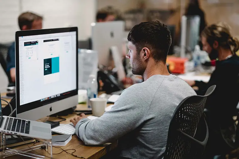 Man in gray shirt sitting on chair in front of iMac