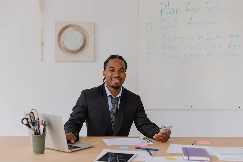 Smiling man with braided hair sitting at desk in an office