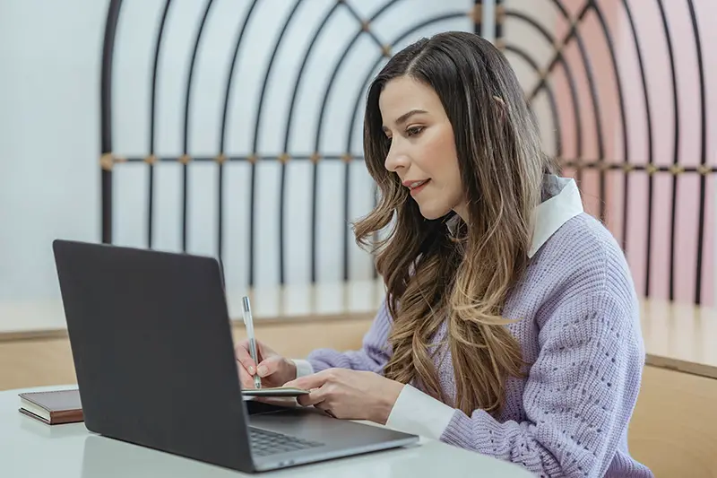 positive woman writing on notebook and watching laptop