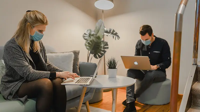 Man and woman working on their laptop while wearing face mask