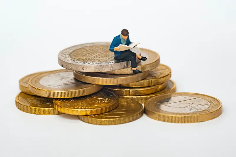 Miniature man sitting while reading on the top of gold coins
