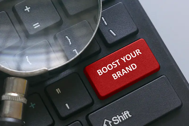 Magnifying glass on a computer keyboard with red button written with advice Boost your brand.