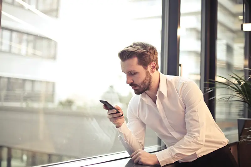 man using mobile phone beside window