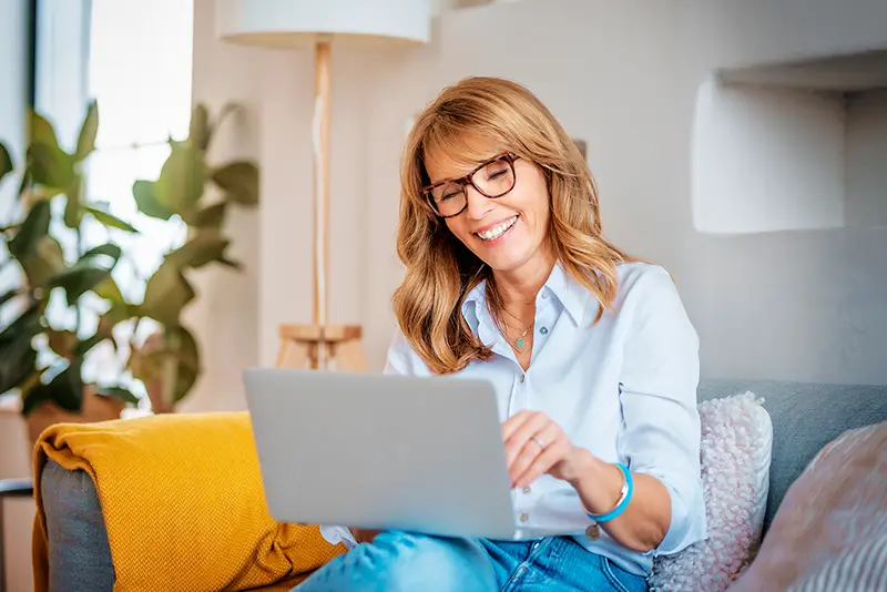 happy middle aged woman using her laptop on the sofa at home