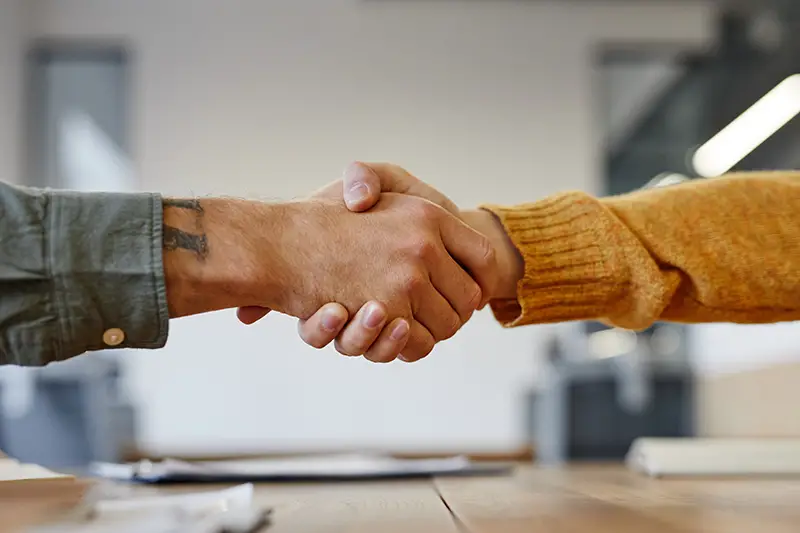 Side view close up of two young men shaking hands at meeting table in office
