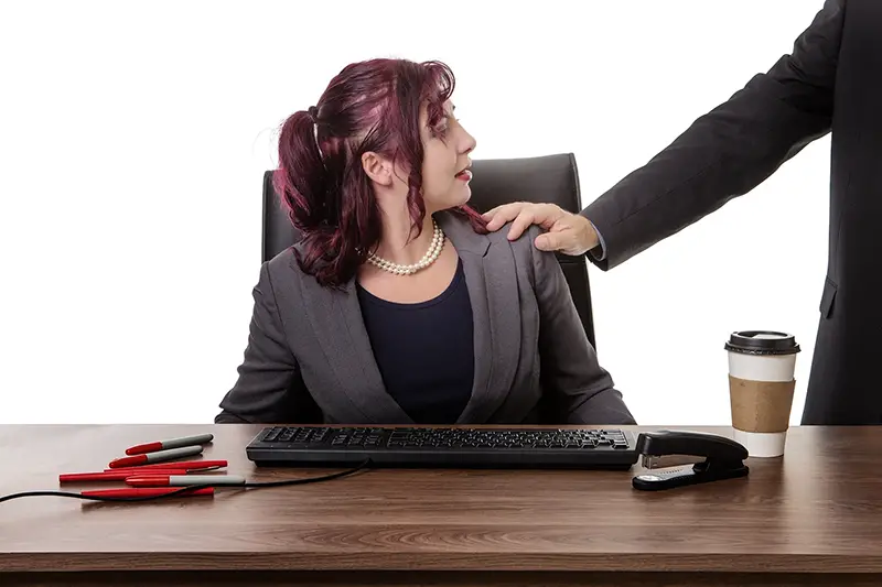 secretary sitting at desk with a mans hand on her shoulder