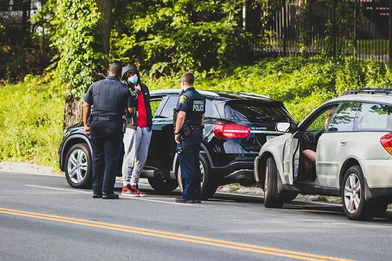 Two policemen talking to a guy near black and gray car