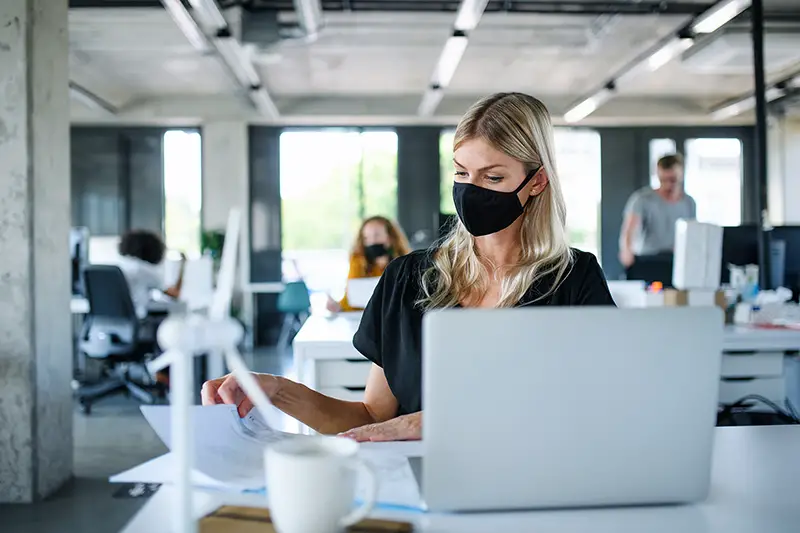 Young woman with face mask back at work in office