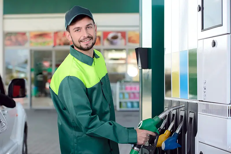 Smiling worker at the gas station, while filling a car