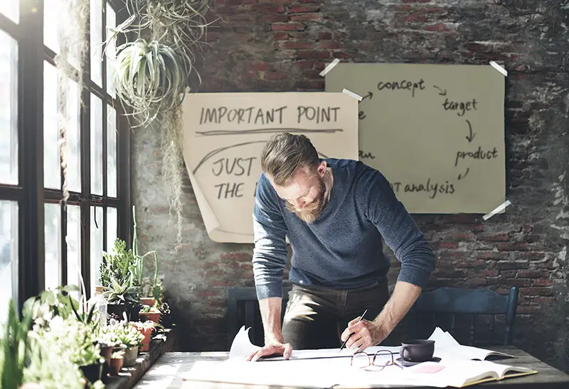 Man wearing blue sweatshirt working while standing in front of his table